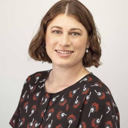 Dr Tahira Bhatti smiles at the camera in front of a white background. She has short brown hair and is wearing a black patterned top.