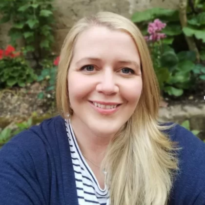 Dr Emily MacDonald smiles at the camera. She has long blonde hair and is wearing a white and blue stripped T-shirt