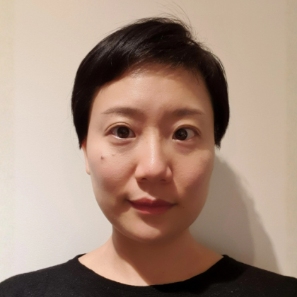 Dr Jun Xiao smiles at the camera in front of a beige background. She has short dark hair and is wearing a black top